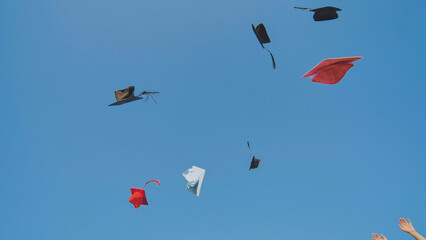Graduates tossing multicolored hats against a blue sky.