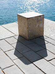 Concrete cube or cement brick with shadow. Abstract photo. Stone cube close-up with blue sea on the...