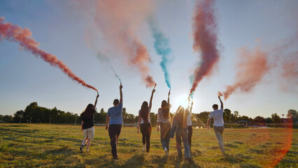 A group of friends spraying multi-colored smoke at sunset.