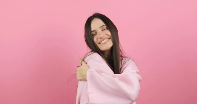 Come into my arms. Adorable happy girl with brown hair in pink dress gesturing come here for free hugs and smiling sincerely with welcoming expression isolated on pink background. Come to me, hug self