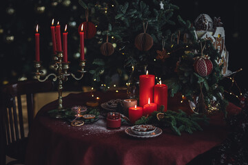 Beautiful elegant table decoration with red candles, fir tree branches with handmade craft toys in...