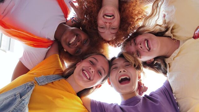 Low angle view of five teenage girls laughing and looking at camera. Group of young women smiling looking down. Real carefree ladies embracing together. Excited friends posing for a photo portrait