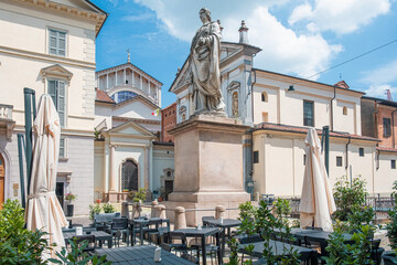 Cafe tables and chairs outside on an old square with a monument in Novara city, Piedmont, Italy. Piazza Puccini with sidewalk cafe in Italian town. Travel destination
