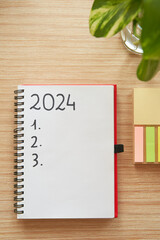 Top view of notebook with 2024 new year's resolutions and goals list by post it and pothos plant...