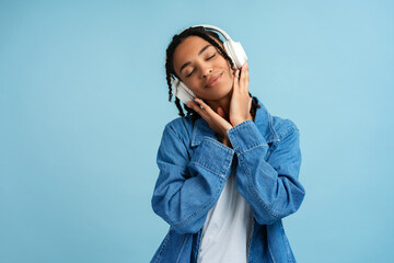 Happy African American woman wearing denim shirt with closed eyes listening to music in headphones - obrazy, fototapety, plakaty