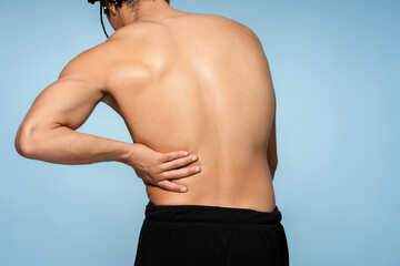 Back view sick man holding hands muscular back, lower back pain, patient standing isolated on blue background