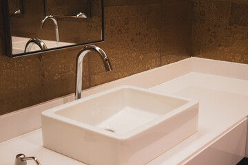 A stainless water tap in a modern bathroom. Metal tap, basin, piping white square sink in modern...