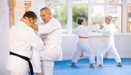 Irate mature male karate practitioner fighting with his opponent in sports hall