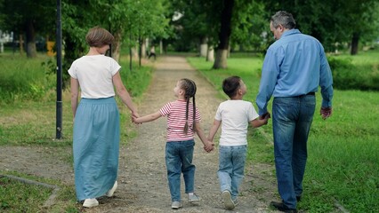 Mom, dad, child, big family. Happy family with three children walks outdoors in city park in summer. Parents children go together, family weekend. Family holiday. People walk in park holding hands.