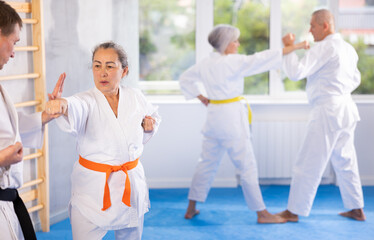 Senior karate practitioner engage in fierce fight, perseverance during martial arts discipline, middle-aged teacher and mature followers. Work on yourself, increase endurance, determination, courage