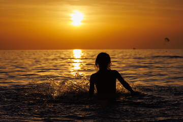 Fototapeta premium Silhouette of a girl in the spray of the sea at sunset.