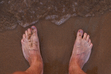 Male feet on sea sand and wave.