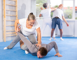 Mature woman learns how to do painful hold with trainer in the gym. Self-defense lesson