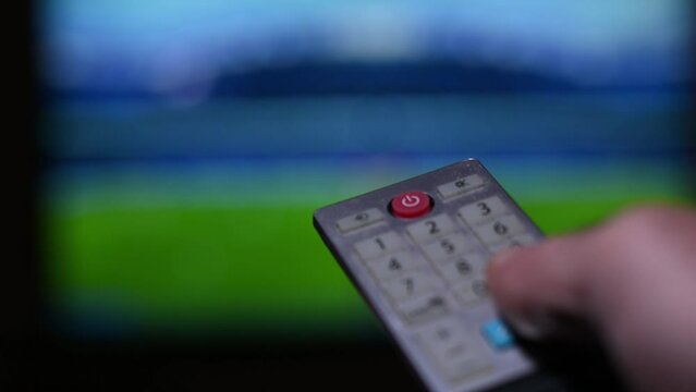 A person is hand presses the television remote control choosing channels with blurred background