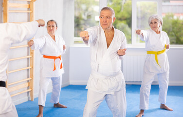 Active mature man wearing kimono training karate techniques in group during workout session