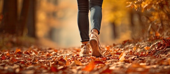 Female legs in hiking shoes walking through autumn leaves on forest path
