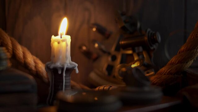 Antique burning candle with vintage sextant, rope and other marine accessories. Sea adventure concept. Selective focus, low shallow focus