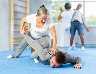 Sportive aged lady practicing arm twist technique against her partner during self-defense courses