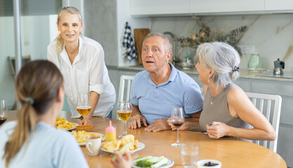 Cheerful mature men and women having jolly conversation with goblets in hands during lunch time