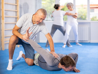 Senior man train in pair with middle-aged coach to strike and reflect blows of enemy. Intense...