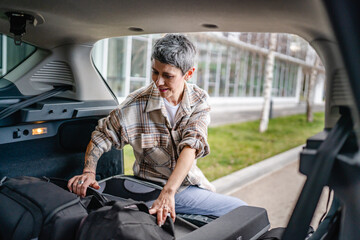 one senior woman pack luggage baggage suitcase in the trunk of the car