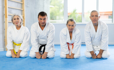 Senior male and female students of Academy of martial Arts together with man teacher sitting on...