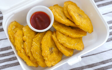 Fried platanos and sauce on plate. Sliced and cooked tostones