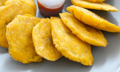 Fried platanos and sauce on plate. Sliced and cooked tostones