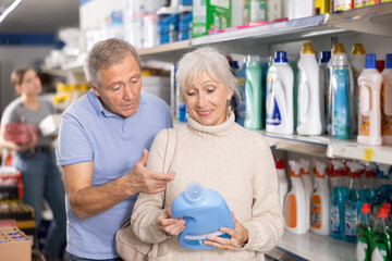 Positive interested elderly couple, man and woman, buying household chemicals in supermarket,...