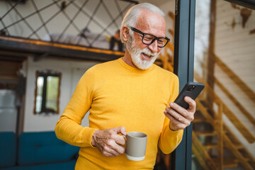 Senior Man Hold cup of coffee and Mobile Phone on Balcony happy smile