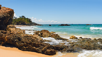 Australian coast with volcanic rocks at the shore on the beach, view from the beach to the horizon with blue water and waves on a summer sunny day.