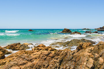 Australian coast with volcanic rocks at the shore, view from the beach to the horizon with blue water with waves on a summer sunny day.