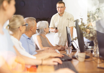 Male IT teacher giving lesson to elderly people in a nursing home - obrazy, fototapety, plakaty