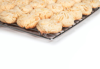 Baked almond flour cookies on cooling rack. Gluten free unbaked raw cookie dough. Group of round cookie with almond slices. GF almond cookies. Selective focus. White background