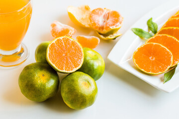 Green and yellow tangerines, one of which was cut in half, were designed on a white background with a glass of tangerine juice
