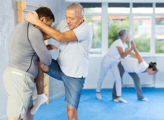 Obraz premium Mature man at a self-defense lesson learns how to make painful blows with his hand and foot