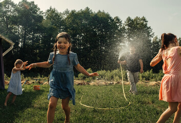 Dad and daughters play in the summer in the garden, a man sprinkles water on his daughters - obrazy, fototapety, plakaty