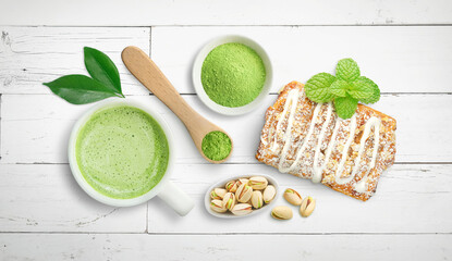 Matcha latte tea display with pistachio nuts and pastry on bright white wood background
