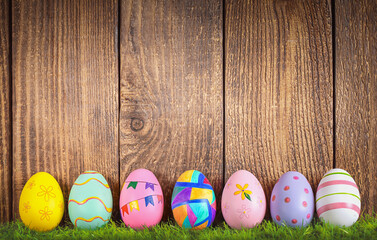Easter background with painted eggs on the grass near a wooden fence