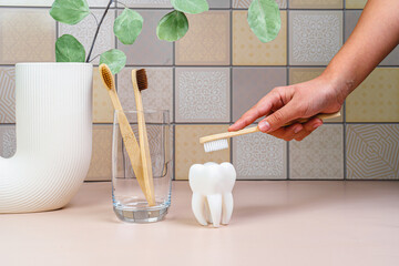 Brushing teeth concept. Bathroom interior, girl holding a toothbrush. Bamboo eco toothbrushes in a...