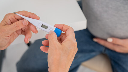 Obraz premium A pregnant woman visits a doctor. Therapist holding an electronic thermometer. 