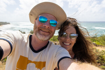 Happy middle aged couple together on vacation at ocean beach. The man and woman are smiling for a selfie overlooking the sea. 