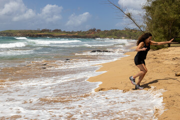 Woman running from the incoming tide on a tropical island beach in Hawaii. 