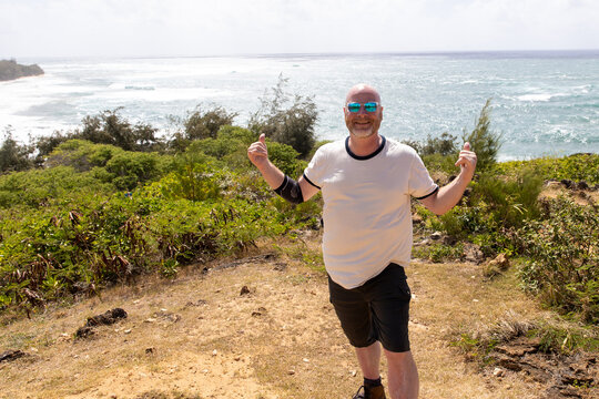 bald man wearing sunglasses on a hike in Hawaii with an elevated view of the Pacific ocean behind him. 