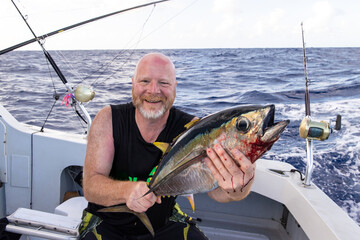 Happy man holding a fresh caught bigeye tuna fish on a fishing boat in the Pacific ocean