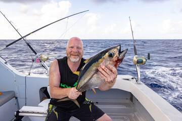 Happy man holding a fresh caught bigeye tuna fish on a small charter boat in Hawaii. 