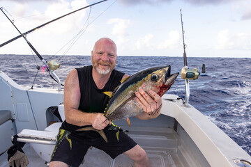 Happy man holding a fresh caught bigeye tuna fish on a small charter boat in Hawaii. 