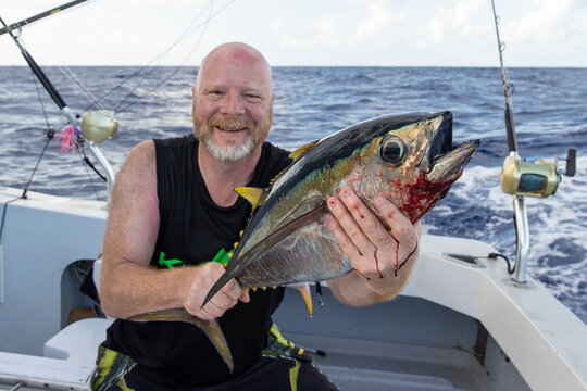 Happy man holding a fresh caught bigeye tuna fish on a small charter boat in Hawaii. 