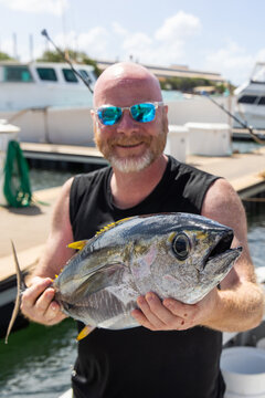 Happy man holding a fresh caught bigeye tuna fish on a small charter boat in Hawaii. 