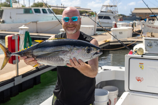 Happy man holding a fresh caught bigeye tuna fish on a small charter boat in Hawaii. 